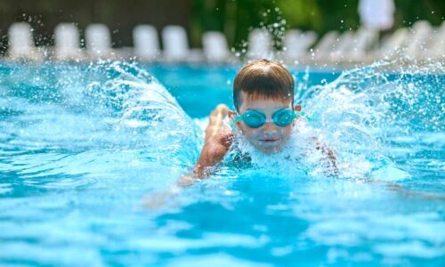 Ein glücklicher Junge mit Taucherbrille der im türkis-farbenen Pool des Mammendorfer Freibads plantscht