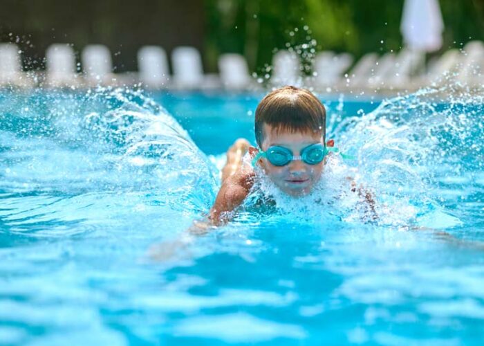 Ein glücklicher Junge mit Taucherbrille der im türkis-farbenen Pool des Mammendorfer Freibads plantscht